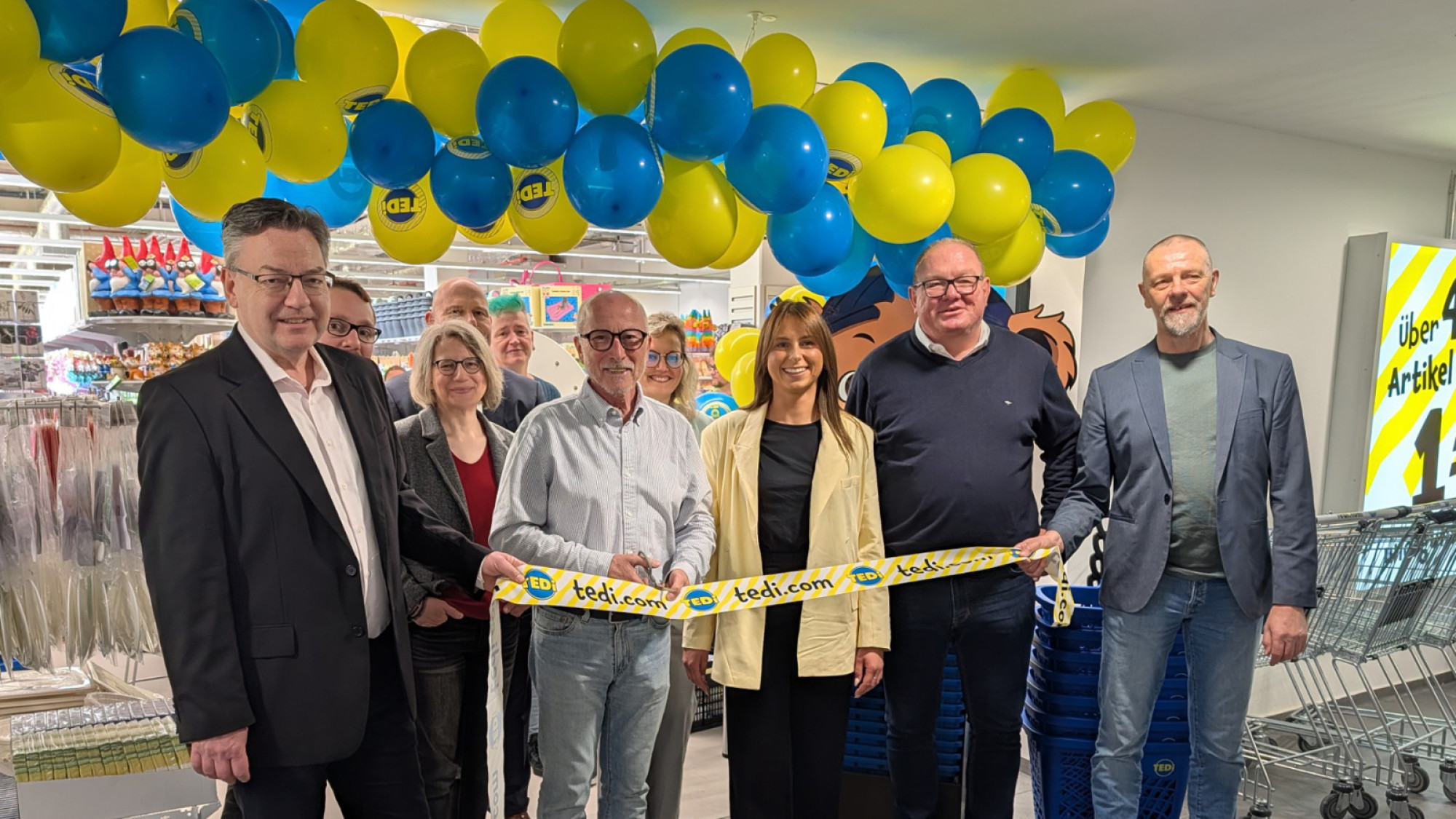 Bürgermeister Fred Toplak (vorne, 2. v. l.) hat die Schere schon zur Banddurchtrennung angesetzt. TEDI freut sich nach der offiziellen Eröffnung am Donnerstag, 16. April, auf seine Kundinnen und Kunden in den Hertener Höfen. (Foto: Stadt Herten_Calina Herzog)